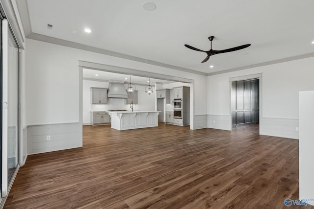 unfurnished living room featuring dark hardwood / wood-style flooring, sink, ornamental molding, and ceiling fan