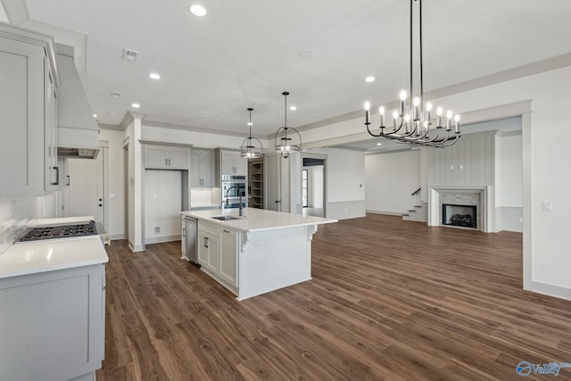 kitchen with decorative light fixtures, stainless steel appliances, dark wood-type flooring, a center island with sink, and custom range hood