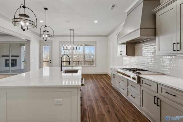 kitchen with tasteful backsplash, hanging light fixtures, a center island with sink, gas cooktop, and custom range hood