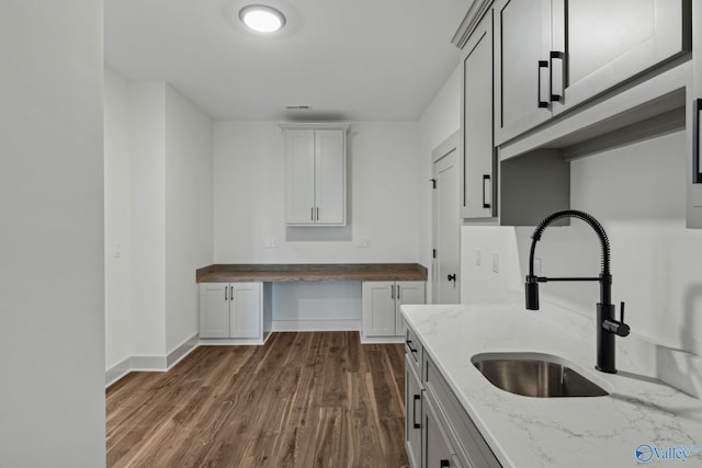 kitchen featuring light stone counters, sink, built in desk, and dark wood-type flooring