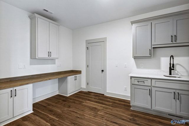 kitchen with built in desk, butcher block countertops, sink, gray cabinetry, and dark wood-type flooring