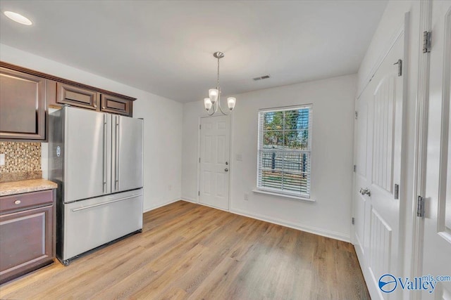 kitchen with decorative backsplash, light countertops, high end refrigerator, light wood-type flooring, and a chandelier