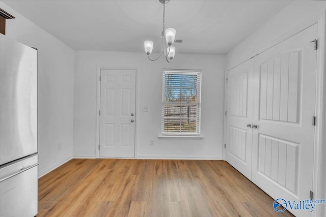 unfurnished dining area with light wood-style flooring, a notable chandelier, and baseboards