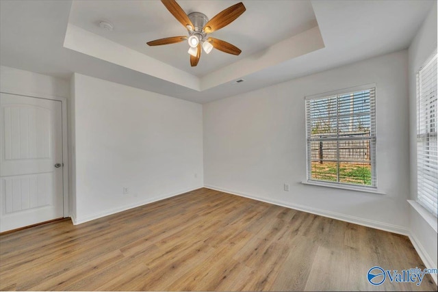 empty room featuring a tray ceiling, baseboards, ceiling fan, and light wood finished floors