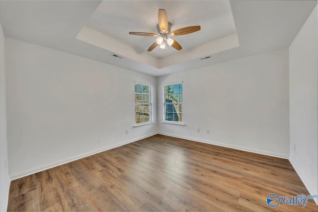 empty room with ceiling fan, a tray ceiling, visible vents, and wood finished floors