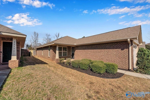 view of property exterior featuring brick siding, a lawn, a shingled roof, and fence