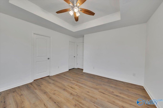 unfurnished room with baseboards, a ceiling fan, a tray ceiling, and wood finished floors