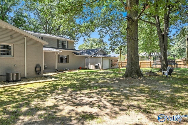 view of yard featuring an outdoor fire pit, central AC unit, fence, and an attached garage