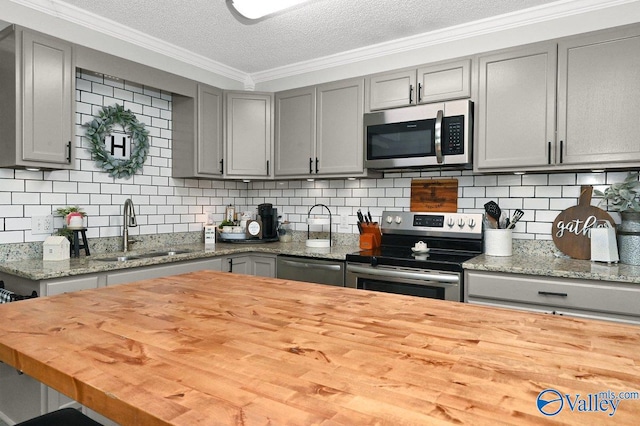 kitchen with butcher block countertops, ornamental molding, stainless steel appliances, gray cabinetry, and a sink