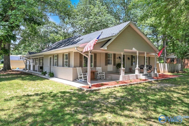 rear view of property featuring a lawn, a shingled roof, and covered porch