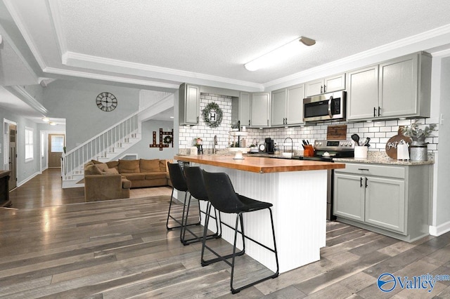 kitchen featuring butcher block countertops, a breakfast bar, dark wood finished floors, appliances with stainless steel finishes, and gray cabinets
