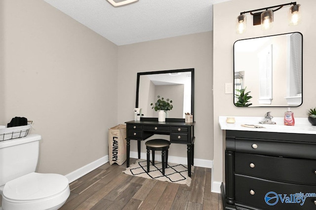 bathroom with toilet, wood finished floors, vanity, and baseboards