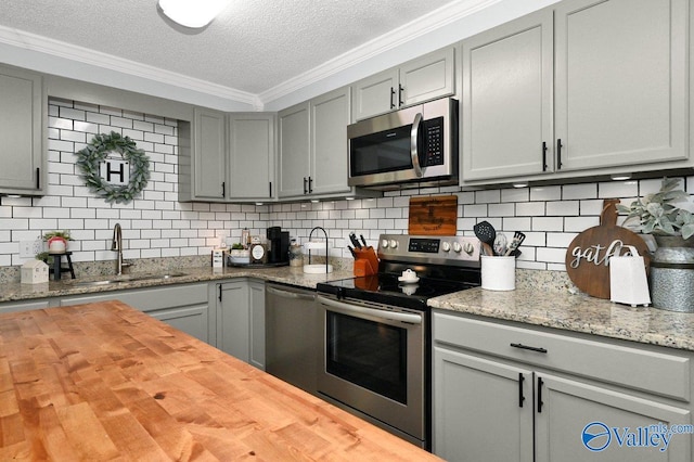 kitchen with gray cabinets, ornamental molding, wooden counters, a sink, and appliances with stainless steel finishes