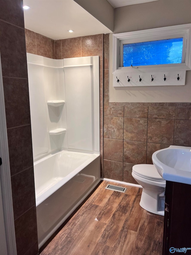 full bathroom with vanity, wood-type flooring, shower / bathing tub combination, tile walls, and toilet