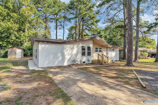 view of front of property featuring crawl space, a storage shed, an outdoor structure, concrete driveway, and entry steps