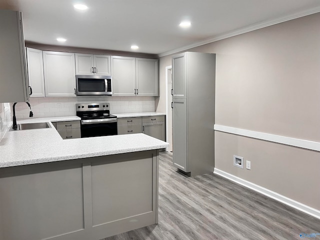 kitchen featuring light wood-type flooring, sink, kitchen peninsula, gray cabinetry, and appliances with stainless steel finishes