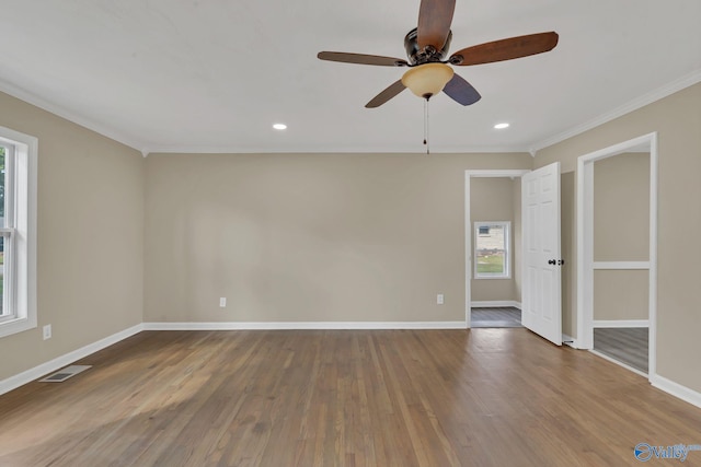 spare room with crown molding, ceiling fan, baseboards, wood finished floors, and visible vents