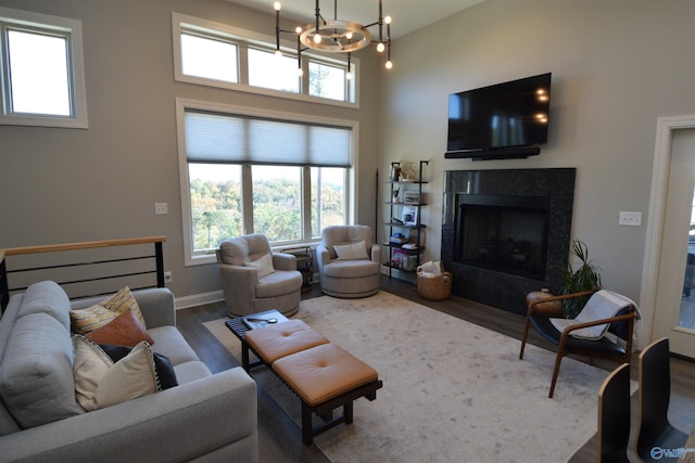 living room featuring a chandelier, a high ceiling, wood-type flooring, and a tile fireplace