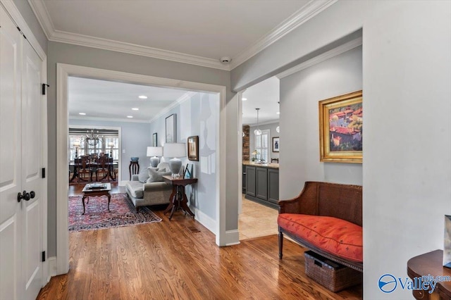 corridor with light wood-type flooring, a chandelier, and ornamental molding