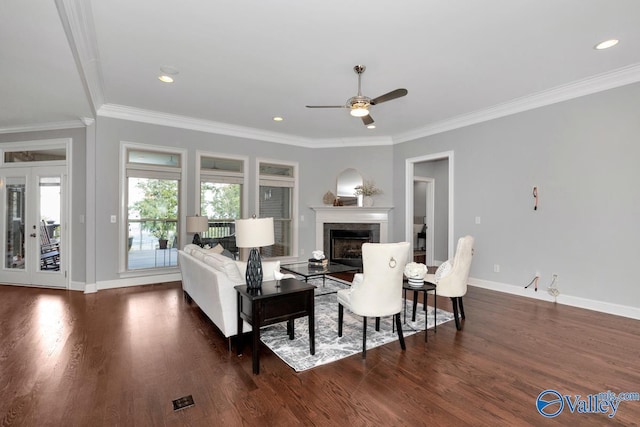 living area with baseboards, dark wood-style flooring, a glass covered fireplace, and crown molding