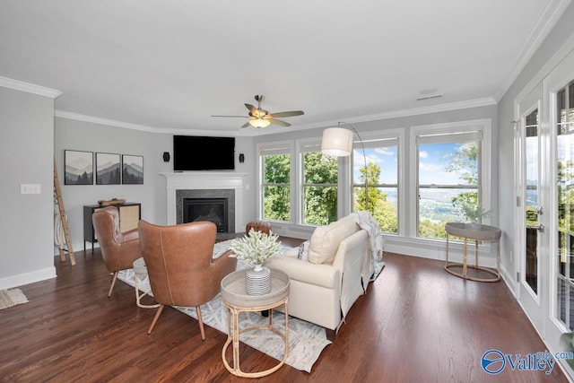 living area featuring baseboards, a ceiling fan, a fireplace with flush hearth, ornamental molding, and dark wood-type flooring