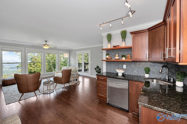 kitchen with tasteful backsplash, dark stone counters, crown molding, open shelves, and a sink