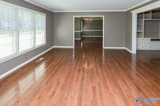 spare room featuring crown molding, wood finished floors, visible vents, and a notable chandelier