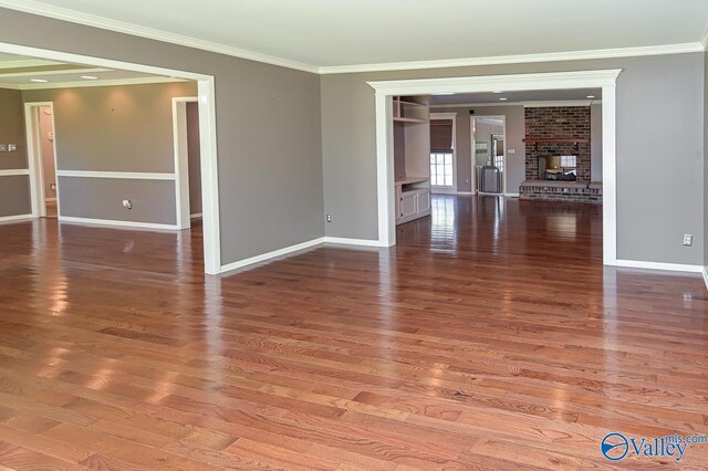 unfurnished room with a brick fireplace, baseboards, ornamental molding, and wood finished floors