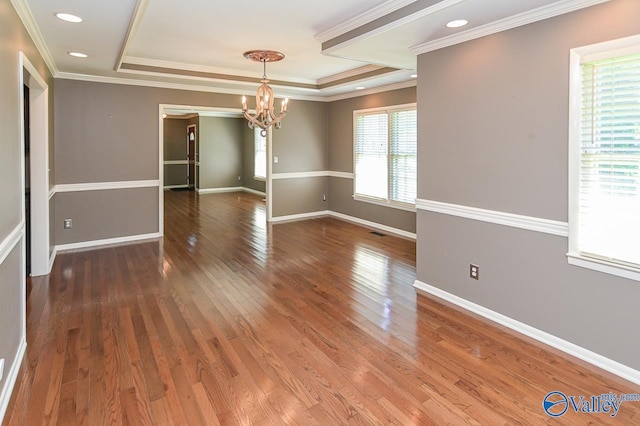 spare room with a raised ceiling, visible vents, baseboards, and wood finished floors