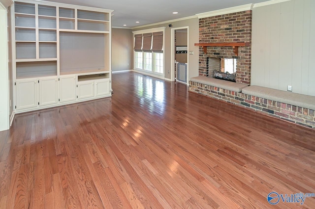 unfurnished living room with baseboards, ornamental molding, wood finished floors, a brick fireplace, and recessed lighting