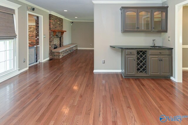 bar featuring a brick fireplace, crown molding, a sink, and wood finished floors