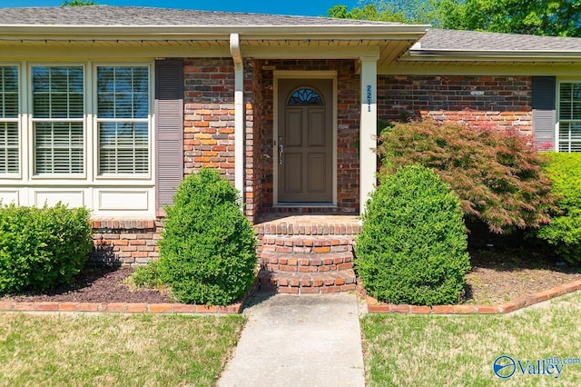 view of exterior entry with brick siding and roof with shingles