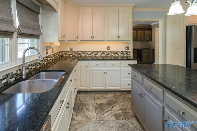 kitchen with crown molding, tasteful backsplash, a sink, dark stone counters, and stainless steel fridge with ice dispenser