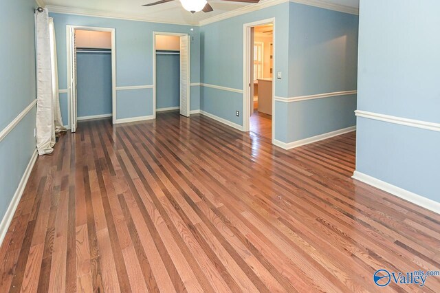 unfurnished bedroom with baseboards, ceiling fan, wood finished floors, crown molding, and two closets