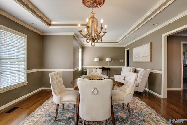 dining space with a tray ceiling, visible vents, wood finished floors, a chandelier, and baseboards