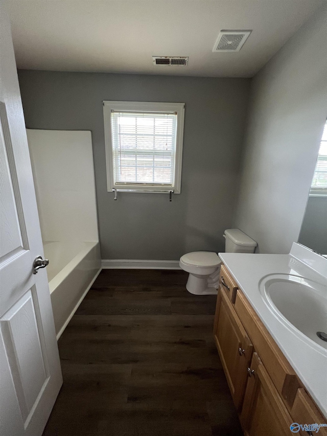 bathroom with hardwood / wood-style flooring, vanity, toilet, and a tub to relax in