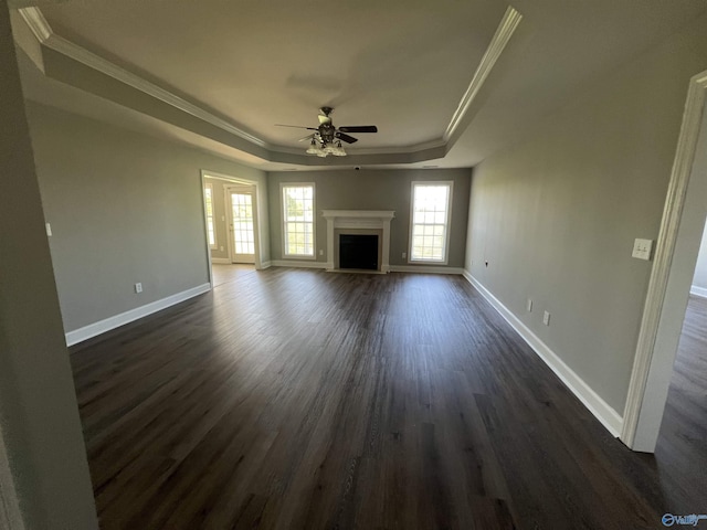 unfurnished living room featuring a tray ceiling, crown molding, ceiling fan, and dark wood-type flooring