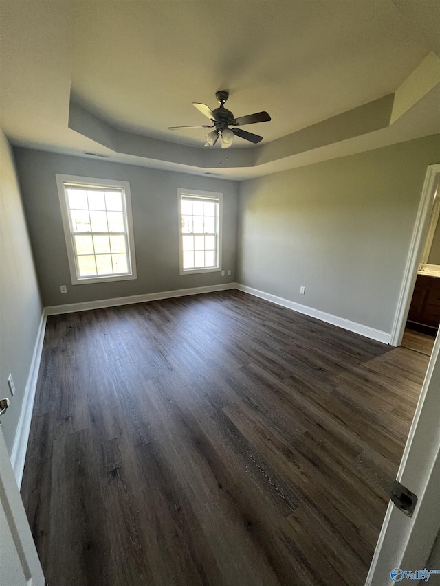 spare room with dark hardwood / wood-style floors, ceiling fan, and a raised ceiling