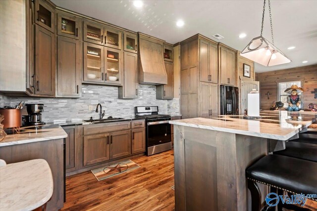 kitchen featuring stainless steel gas range oven, a sink, black refrigerator with ice dispenser, a kitchen bar, and custom range hood