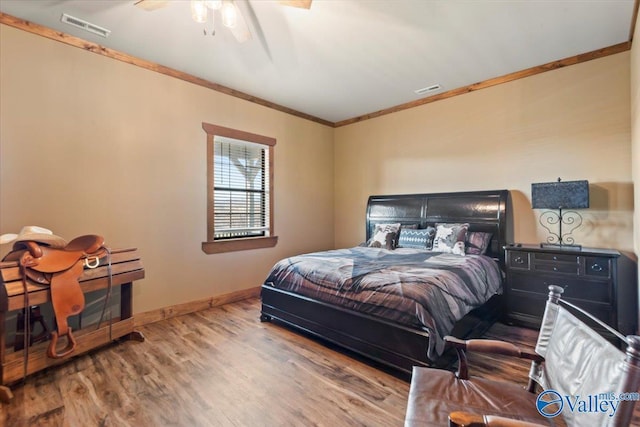 bedroom with baseboards, wood finished floors, visible vents, and crown molding