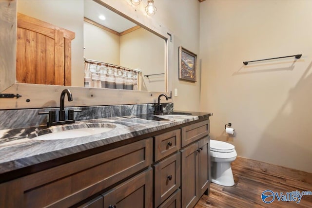 bathroom featuring double vanity, a sink, toilet, and wood finished floors