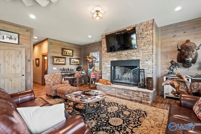 living area featuring wood walls, recessed lighting, wood finished floors, and a stone fireplace