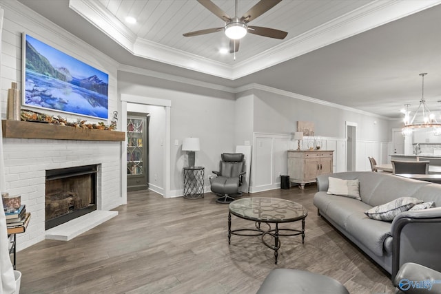 living room with a raised ceiling, ornamental molding, ceiling fan with notable chandelier, and a brick fireplace