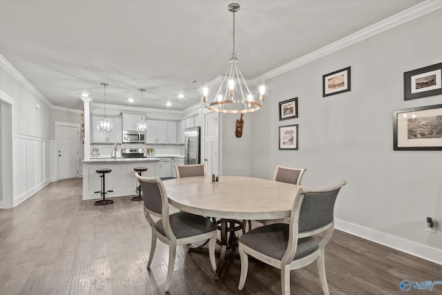 dining space with sink, light wood-type flooring, crown molding, and a chandelier