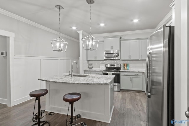 kitchen with sink, light stone countertops, an island with sink, appliances with stainless steel finishes, and decorative light fixtures