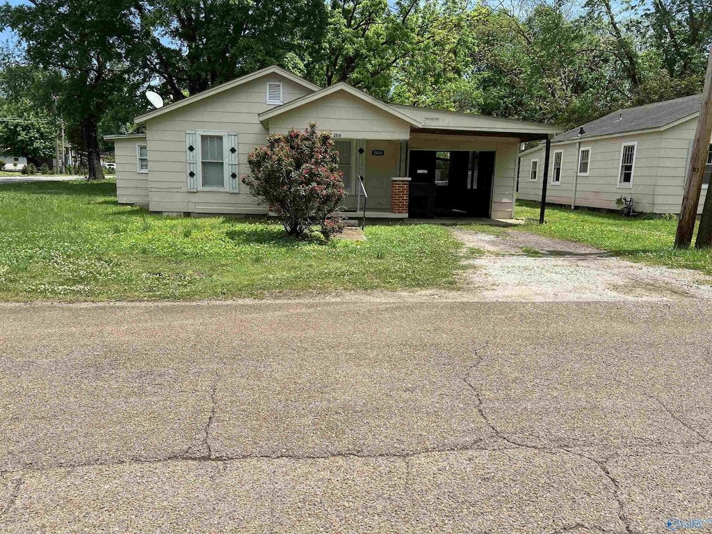 bungalow with dirt driveway, a carport, and a front yard