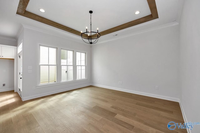 spare room with a raised ceiling, wood-type flooring, crown molding, and a chandelier