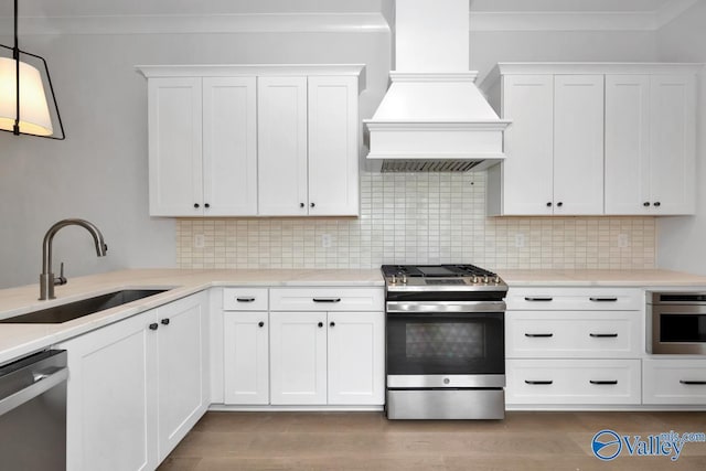 kitchen featuring sink, appliances with stainless steel finishes, custom range hood, pendant lighting, and white cabinets