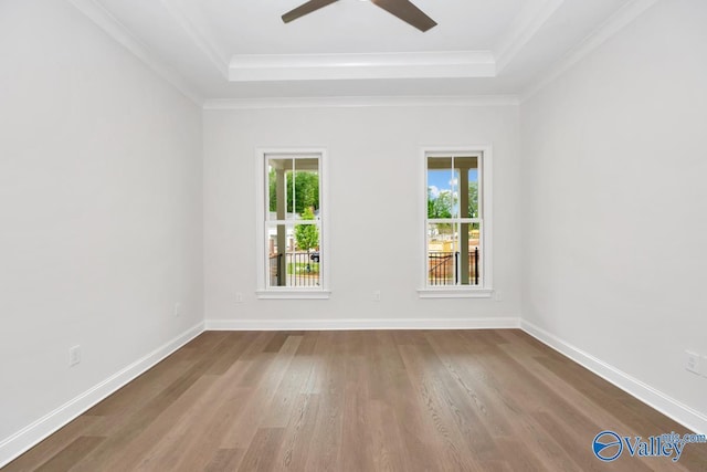 empty room with a raised ceiling, ornamental molding, hardwood / wood-style flooring, and ceiling fan