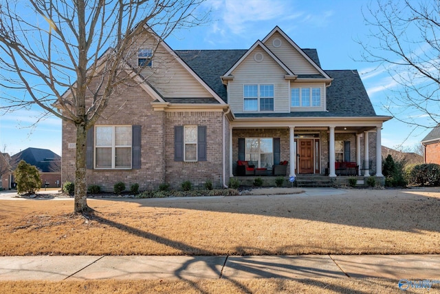 craftsman-style home featuring covered porch, roof with shingles, and brick siding